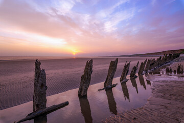 Reflections of wooden groynes with the sun setting  in a peach and blue sky