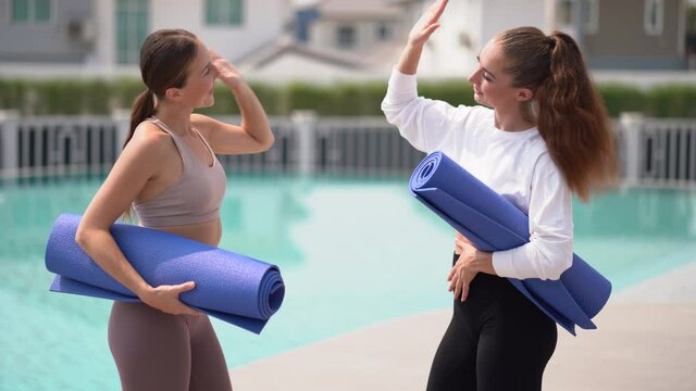 group of fitness woman holding yoga mat greeting with high five after exercising  yoga class by swimming pool outdoors . Group of fit people talking and relaxing in sport club after workout training