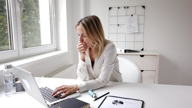 Coughing businesswoman using inhalator in home office