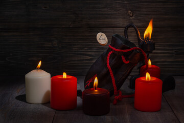 Rune Kenaz. A composition of burning candles, an old leather bag for Scandinavian runes with a bokeh effect.