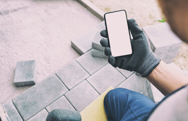bricklayer holding the phone with blank screen in hand on gloves.  mockup for house repair or...
