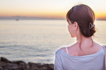 back view of a girl standing on the embankment and enjoying beautiful sunset at the sea