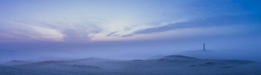 A lighthouse at dawn in the mist and fog under a purple sky