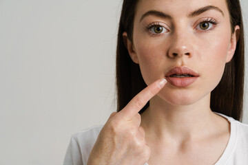 Young woman pointing finger at her mouth and looking at camera