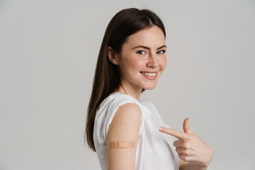 Young brunette woman smiling while pointing finger at her bandage