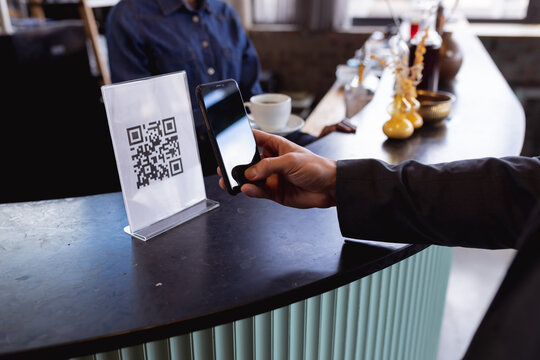 Mid section of man making a payment by scanning qr code from smartphone at a cafe - Powered by Adobe