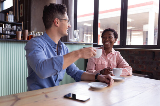 Mixed race couple holding coffee cups smiling while sitting at a cafe