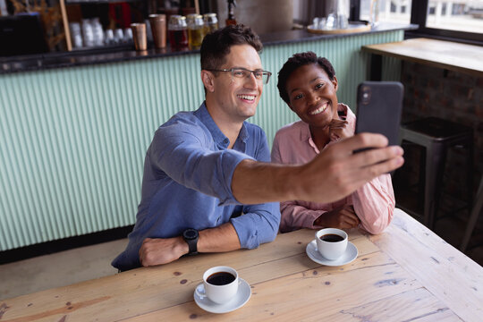 Mid section of mixed race couple smiling while taking a selfie while having coffee at a cafe