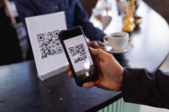 Mid section of man making a payment by scanning qr code from smartphone at a cafe