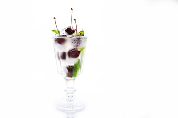 Fresh cherries with ice cubes in a glass. Basil leaves. Cherry lemonade in a transparent glass. Copy space. White background.Refreshing drink.