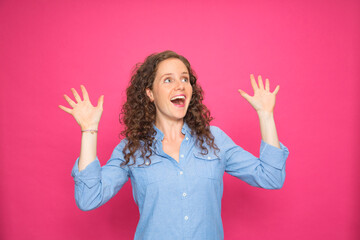 Portrait happy young pretty girl with arms up screaming wearing blue shirt on pink background