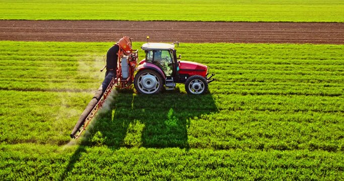 Tractor with pesticide tank spraying crop on field