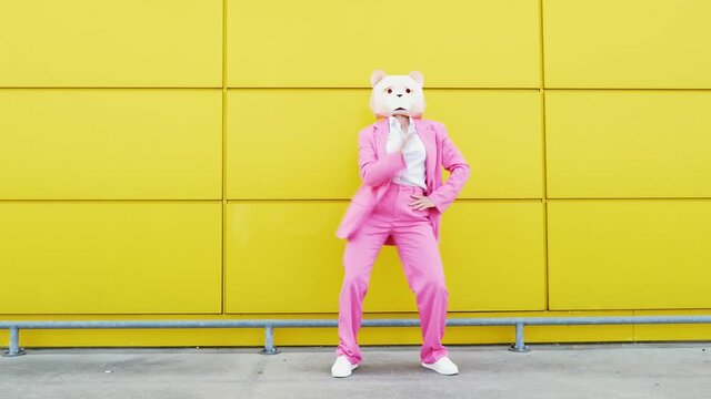 Woman in pink business suit and bear mask dancing in front of wall