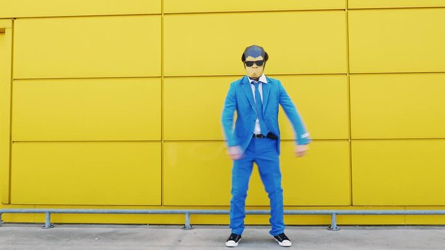 Cool businessman in monkey mask dancing in front of yellow wall
