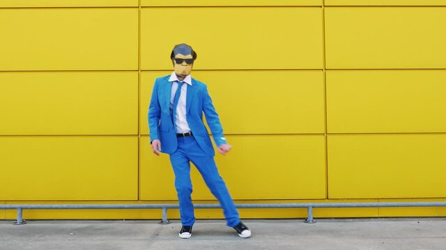 Cool businessman in monkey mask dancing in front of yellow wall