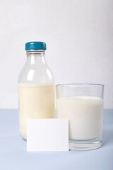 Bootle and glass of milk, white card for information about milk on the blue surface agaist white wall