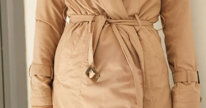 Woman binding belt of trenchcoat, mid section
