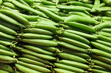 green fava beans in pods on counter in market