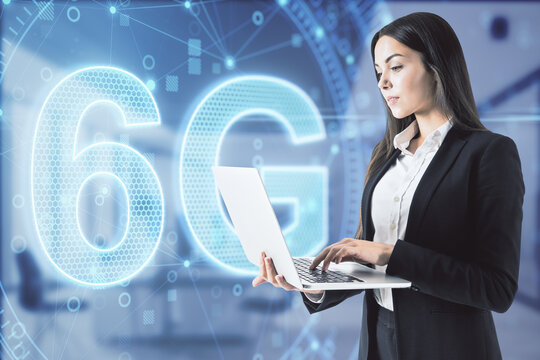 Attractive businesswoman in blurry office using laptop with 6G network digital hologram and internet of things background. High speed internet concept. Double exposure.