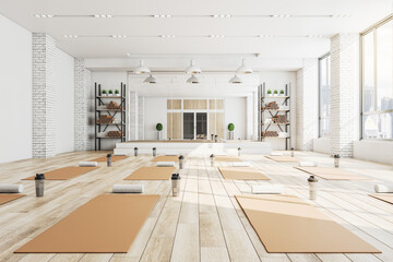 Modern concrete yoga gym interior with equipment, daylight and wooden flooring. Healthy lifestyle...