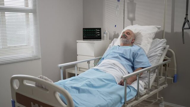 Senior male patient lying in a hospital bed wearing oxygen mask. The device shows the heart rate, pulse, oxygen in the blood, ecg