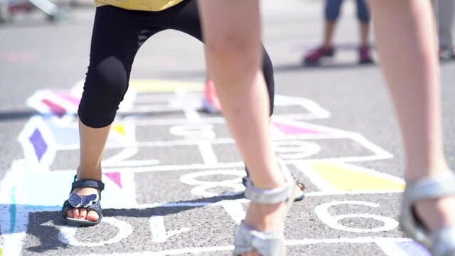 The child plays street games. Kid jumping into classics on the street. The girl happily jumps over the numbers