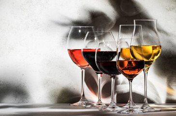Wines assortment. Red, white, rose wine in wineglasses on gray background. Wine tasting concept. Hard sunlight and shadows from foliage