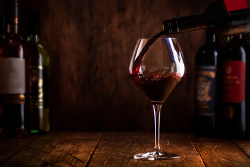 Wine tasting. Red wine pouring into glass on wooden background with selection of red, white and rose wines in bottles