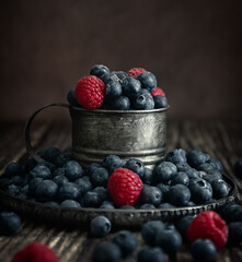 Blueberries and raspberries in a vintage cup on a dark background. Photo in Rustic style. Postcard. High quality photo