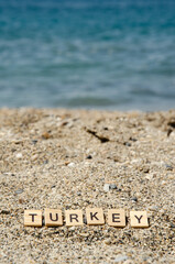 Fototapeta na wymiar Lettering Turkey on sandy beach against background of blurred turquoise sea. Inscription Turkey. Sea vacation concept. Representation of country resorts. Coast is made of small and large stones.