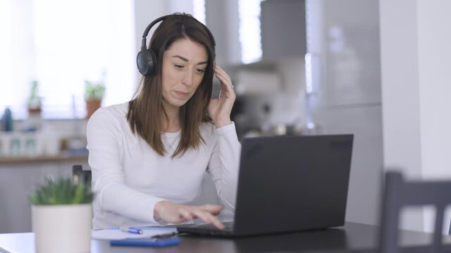 Woman putting on headphones for video call on laptop