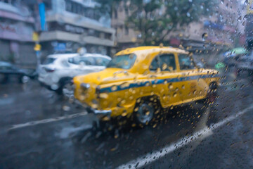 Raindrops falling on glass, abstract blurs - monsoon stock image of traditional yellow taxi of Kolkata (formerly Calcutta) city , West Bengal, India