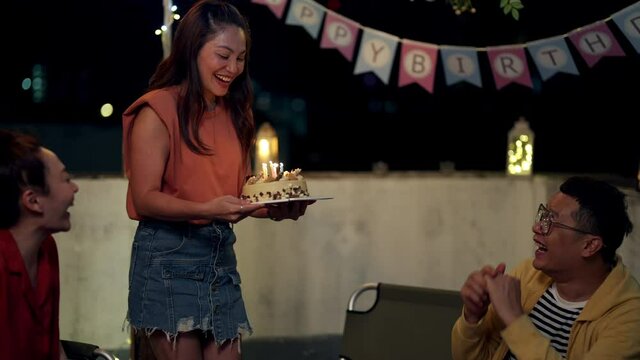 Diversity Asian millennial people friends enjoy outdoor celebration birthday party together with food and drink. Smiling LGBTQ guy excited with birthday cake and blowing birthday candle with happiness