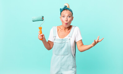 pretty blond woman feeling extremely shocked and surprised and painting a wall