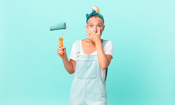pretty blond woman covering mouth with hands with a shocked and painting a wall