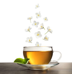 Beautiful jasmine flowers falling into cup of hot freshly brewed tea on white background