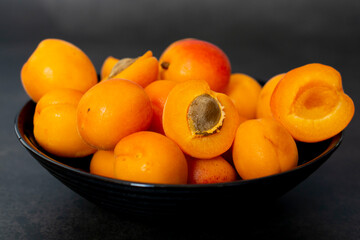 Fresh juicy apricots in the black bowl on the dark background. Close up, top view. Ripe fruits shot with copy space. Cut apricot. Summer fruits background. 
