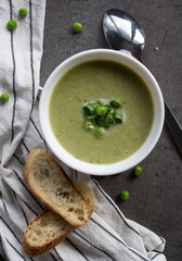 Creamy soup made of green peas with fresh baguette bread and  silver spoon on a table. Balanced diet concept. Top view photo of delicious vegetarian soup. 