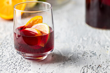 Close up of sangria drink in glass with ice and fruit on white concrete background