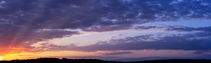 Panorama of a beautiful sunset with purple clouds and sunbeams to the horizon