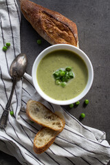 Creamy soup made of green peas with fresh baguette bread and  silver spoon on a table. Balanced diet concept. Top view photo of delicious vegetarian soup. 