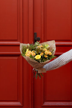 Hand Holding A Bouquet Of Assorted Yellow Flowers In Front Of A Red Door