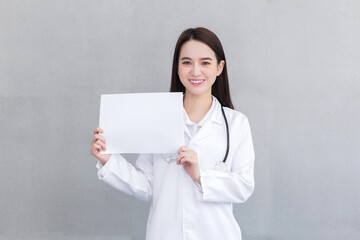 Asian professional doctor woman who wears medical coat holds and shows white paper to present something in healthcare concept.