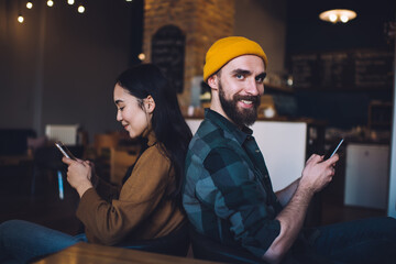 Portrait of cheerful male user with smartphone device in hand smiling at camera while female friend browsing booking website on mobile, millennial hipster guys connecting to 4g for reading content