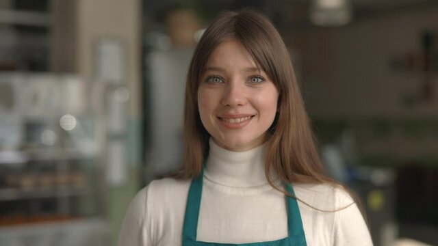 Female cafe worker in apron smiling and looking at camera