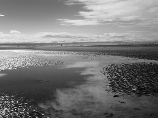 the beach at blundell sands near southport with water from the incoming tide reflecting clouds and sky