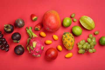 Many different delicious exotic fruits on red background, flat lay