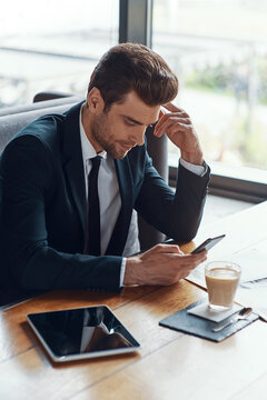 Busy young businessman in full suit using smart phone while sitting in the restaurant