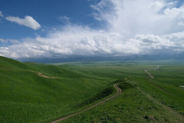 wide green hills with winding long path under white cloudscape. At Nalati prairie in Xinjiang China