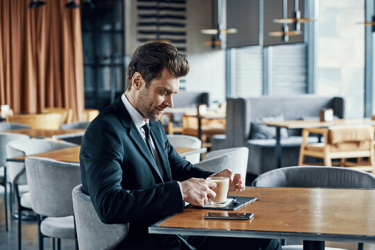 Handsome young businessman in full suit enjoying coffee and smiling while sitting in the restaurant